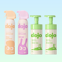 Four Dojo body care products arranged on a pale blue gradient background: two spray bottles labeled Vanilla Sandalwood and Candy Rush, and two pump bottles labeled Pistachio and Pistachio Vanilla.